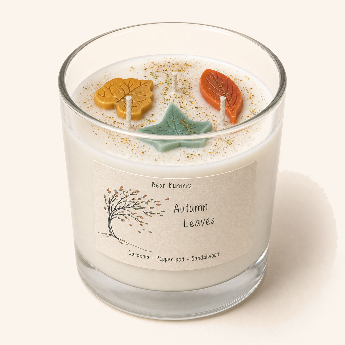 Autumn Leaves candle in a wide clear glass vessel with three wicks and colourful wax leaves on top.