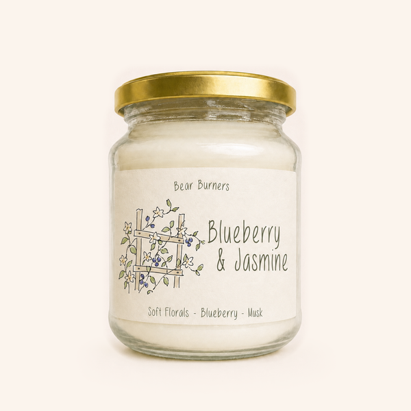 Blueberry & Jasmine candle in a clear glass jar with a gold lid and illustrated cream label.