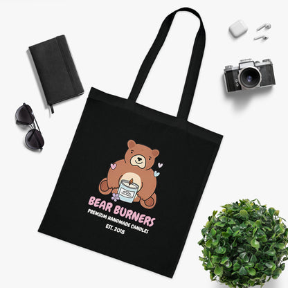 Black Bear Burners tote in a flat lay with a camera, notebook and sunglasses.