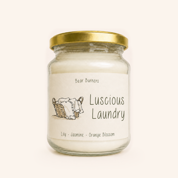Luscious Laundry candle in a clear glass jar with a gold lid and illustrated cream label.