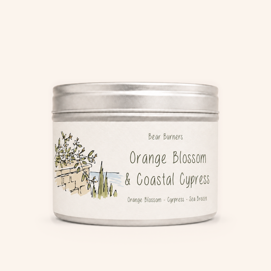 Orange Blossom & Coastal Cypress candle in a silver lidded tin with an illustrated cream label.