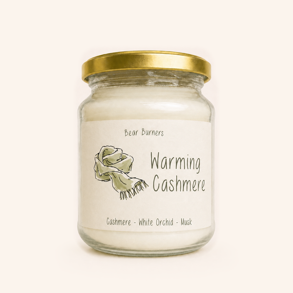 Warming Cashmere candle in a clear glass jar with a gold lid and illustrated cream label.
