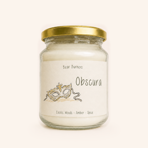 Obscura candle in a clear glass jar with a gold lid and illustrated cream label.